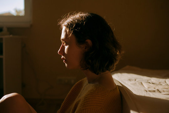 Thoughtful young woman sitting besides bed at home