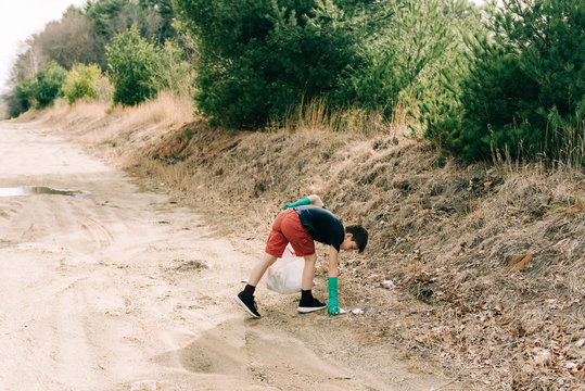 stock photo of little boy picking up trash on the side of the road for earth day