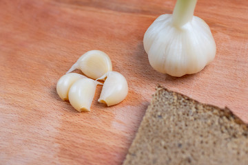garlic soaked in a special sauce. next to a piece of dark rye bread. close-up. on a wooden background.