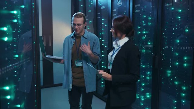 IT technician with female engineer starting a dance moving with laptop inside server rack corridor having fun together. Comical team of data center. Concept of humor.