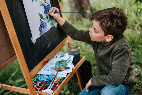 A young boy draws in the open air in the spring