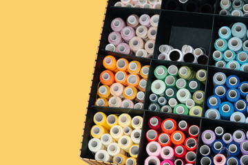 Set of color sewing threads in cardboard compartment box on yellow background
