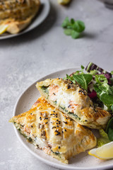 Puff pastry pie with salmon, spinach and ricotta cheese served with green lettuce leaves. Salmon Wellington in puff pastry.