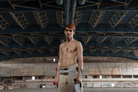 portrait of a guy disabled on crutches in an abandoned gym without a t-shirt