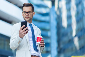 Business man reading sms on phone and holding cup of coffee