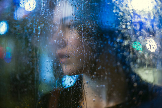 Portrait of young woman looking through wet glass