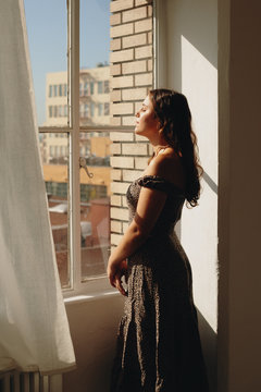 Young woman standing by window with eyes closed