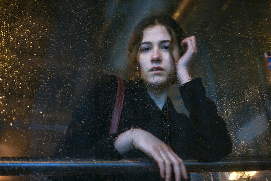 Portrait of young woman looking through wet glass