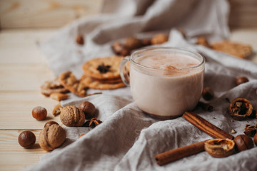 Hot cocoa with cookies, cinnamon sticks, anise, nuts on wooden background. Front view.