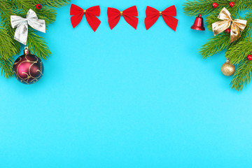 Fototapeta na wymiar Christmas border with branches of spruce, holidays bows, christmas toys on a blue background. The concept of winter holidays: New Year, Christmas. Layout with copy space for your text.