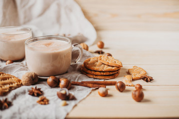 Hot cocoa with cookies, cinnamon sticks, anise, nuts on wooden background. Front view.
