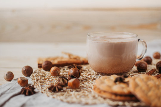 Hot cocoa with cookies, cinnamon sticks, anise, nuts on wooden background. 