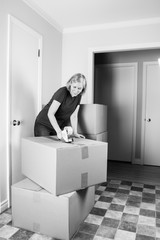 Mature woman prepares to move to another house closing boxes with tape