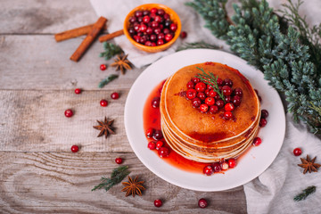 Stack of american pancakes with fresh cranberry and jam in white plate on wooden rustic table decorated Christmas tree, delicious dessert for breakfast in winter, vintage style. 
