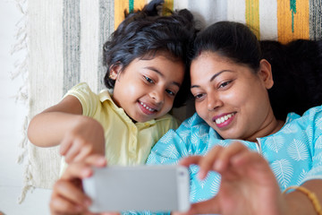 Mother and daughter taking selfie with mobile phone lying on a rug