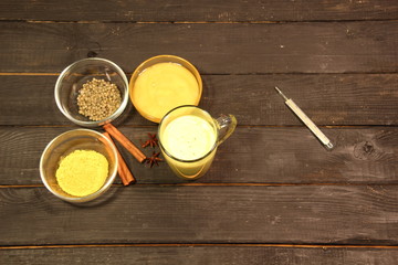 Golden milk made with turmeric, pepper, honey, cinnamon, anis on black wooden background agains thermometer and disease