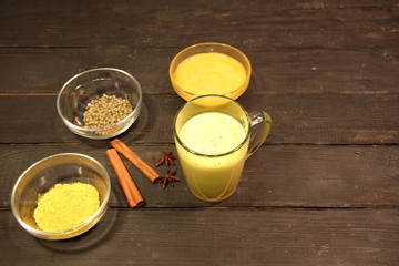 Golden milk in glass cup made with turmeric, pepper, honey, cinnamon, anis on black wooden background