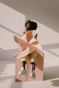 Cheerful black woman with pinwheel sitting on cube