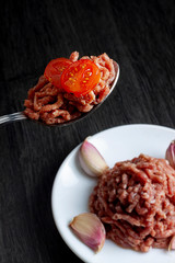 SPICY MEAT IN SPOON WITH TOMATO CHERRY AND DISH WITH REST OF MEAT WITH GARLIC. STEAK TARTARE
