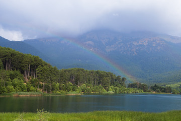 Mountain landscape. View of the blue, clean, lake Doxa and trees with rainbow (Greece, region Corinthia, Peloponnese) on a summer, sunny day.