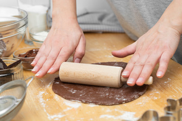 Female hands rolling chocolate dough with rolling-pin. Cooking homemade cookies or pastry, dessert.