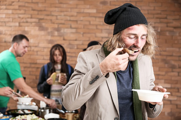 Hungry homeless man eating food received from volunteers