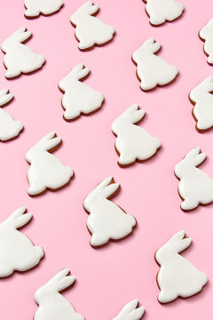 Creative pattern of homemade cookies in the shape of a rabbit with white icing on a pink background. Easter layout. Flat lay