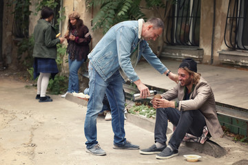 Volunteer giving drink to homeless man outdoors