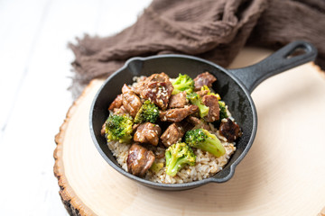 Beef and broccoli over rice in a black skillet topped with sesame seeds 