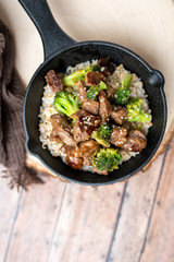 Beef and broccoli over rice in a black skillet topped with sesame seeds 