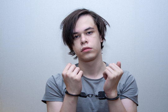A handcuffed teenager sits on a grey background. Juvenile delinquent, criminal liability of minors. Members of youth criminal groups and gangs.