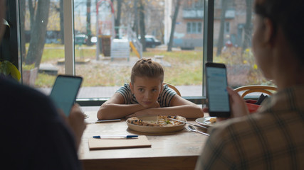 Sad girl looks at her parents sitting in their phones