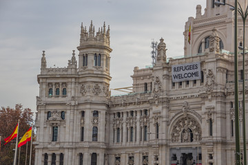 Fototapeta na wymiar Welcome Refugee message on Palacio de Cibeles in Madrid with spain flags