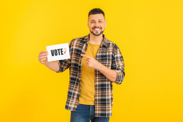 Man holding paper with text VOTE on color background