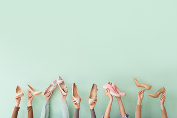 Many hands with different stylish shoes on color background