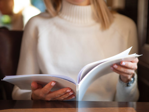 Woman reading a blank white magazine in caffe. Cropped body no face