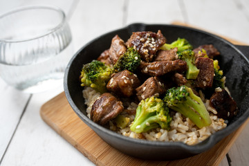 Beef and broccoli over rice in a black skillet topped with sesame seeds 