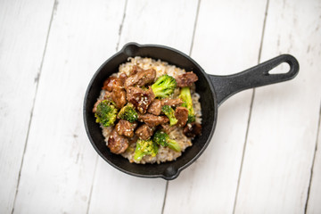 Beef and broccoli over rice in a black skillet topped with sesame seeds 