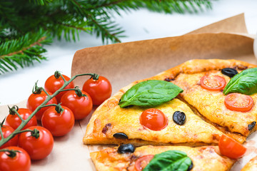 Pizza with tomatoes and spinach on a white background and Christmas fir branches