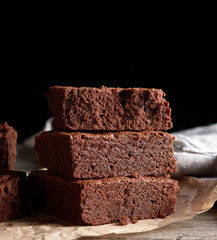 stack of baked square pieces of chocolate brownie cake on brown wooden cutting board