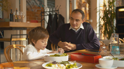 Father and son sit at wooden table and talk