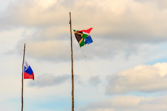Flag of Russia and South Africa on wooden flagpoles on background of blue sky with white clouds. South Africa and Russia flag waving in wind against cloudy together. Diplomacy concept, international