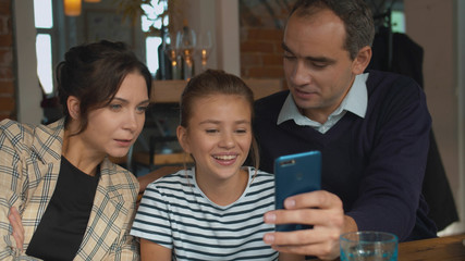 Parents and daughter look at photo on phone in a cafe