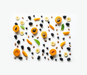 Delicious fruit and berry background. Sliced ​​banana, apricot halves, nuts, blackberries and grapes on a white background.