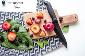 Creative layout of whole and sliced plums, cutting board and tablecloth.