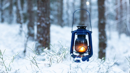Vintage hand lantern a wooden stump in the woods during the winter season. Christmas theme.  Hiking, wilderness and peace concepts. Copy space.