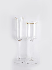 Two clean new transparent glasses with a gold rim for champagne or wine on a white background. Dishes for a party or celebration.