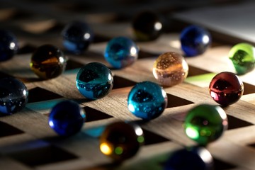 A portrait of a lot of different marbles in different colors, lying on a wooden roster casting a...
