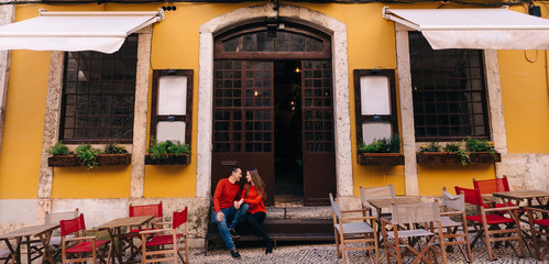 Obraz premium couple in red sweaters sitting on stairs at cafe entrance. many