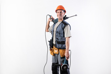 A builder with a hammer drill on his shoulder, and a angle grinder in his other hand, in a helmet,...